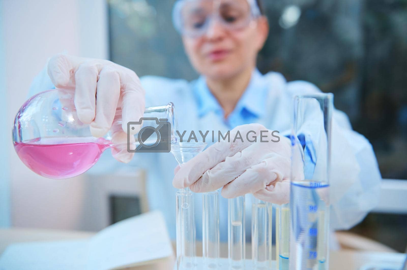 Royalty free image of Close-up. Hands of a scientific researcher pouring liquid through a funnel from a glass laboratory flask into test tubes by artgf