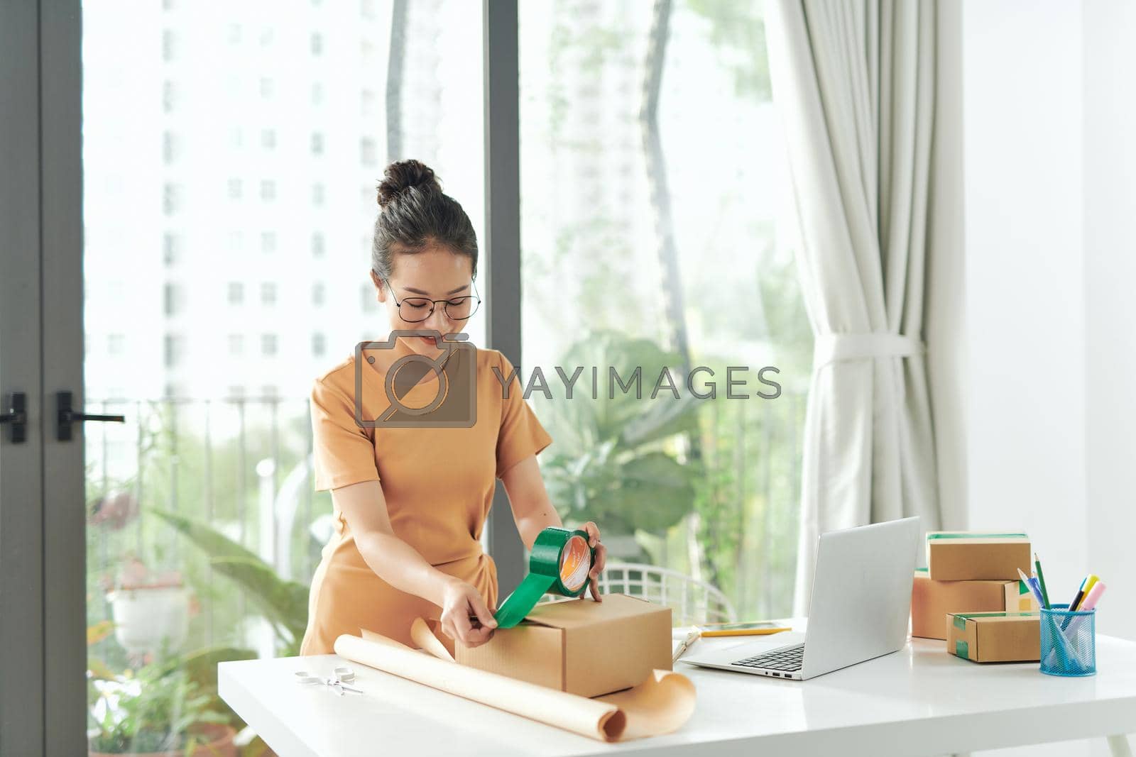 Royalty free image of Startup small business owner working at home, women sealing cardboard box with adhesive tape, by makidotvn