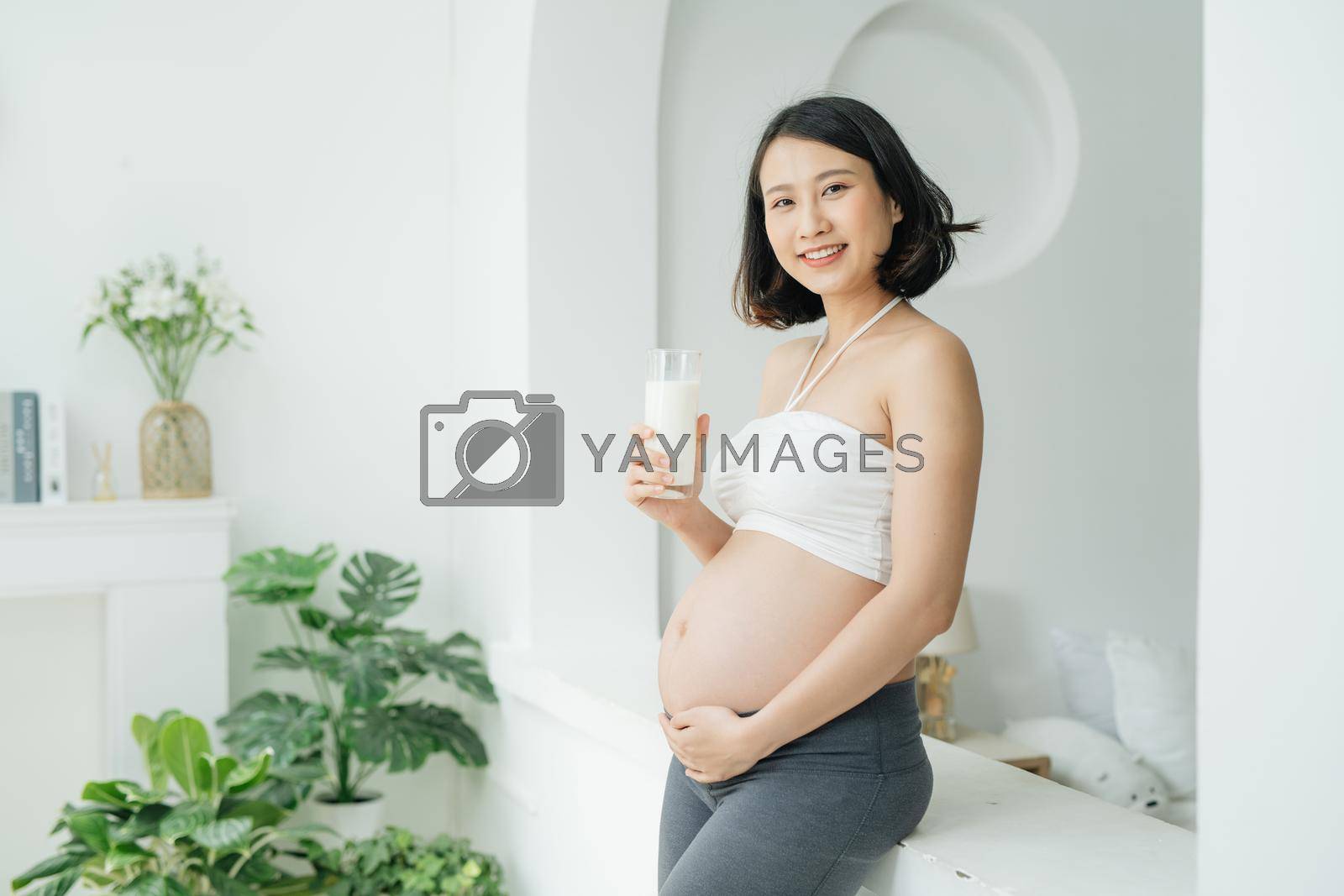 Royalty free image of Beautiful pregnant woman drinking milk at home by makidotvn