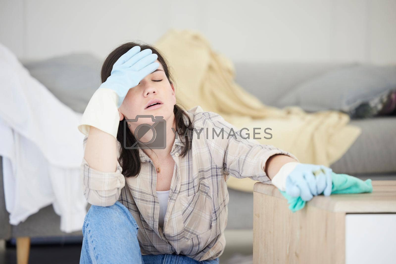 Royalty free image of Tired, stressed young woman with headache doing spring cleaning chores, sitting in her living room at home. Frustrated, overworked female is exhausted from hygienic domestic housekeeping service by YuriArcurs