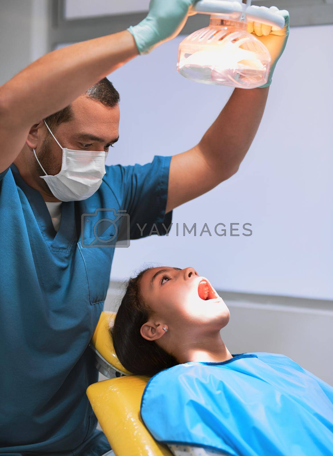 Royalty free image of Shining brightly. a young little girl lying down on a dentist chair with her mouth wide open while the dentist shines a light on her. by YuriArcurs