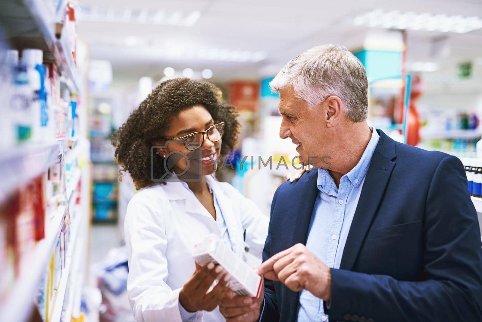 Royalty free image of Do you need help sir. a helpful young female pharmacist helping a customer with choosing the right medication in the pharmacy. by YuriArcurs
