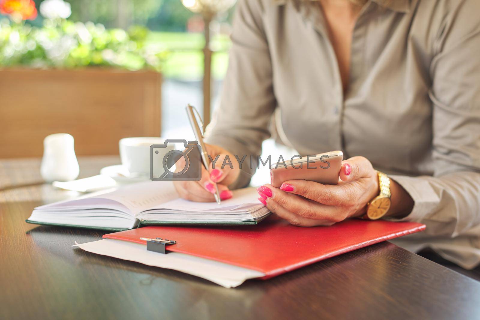 Royalty free image of Businesswoman writing in notebook using smartphone, coffee break by VH-studio