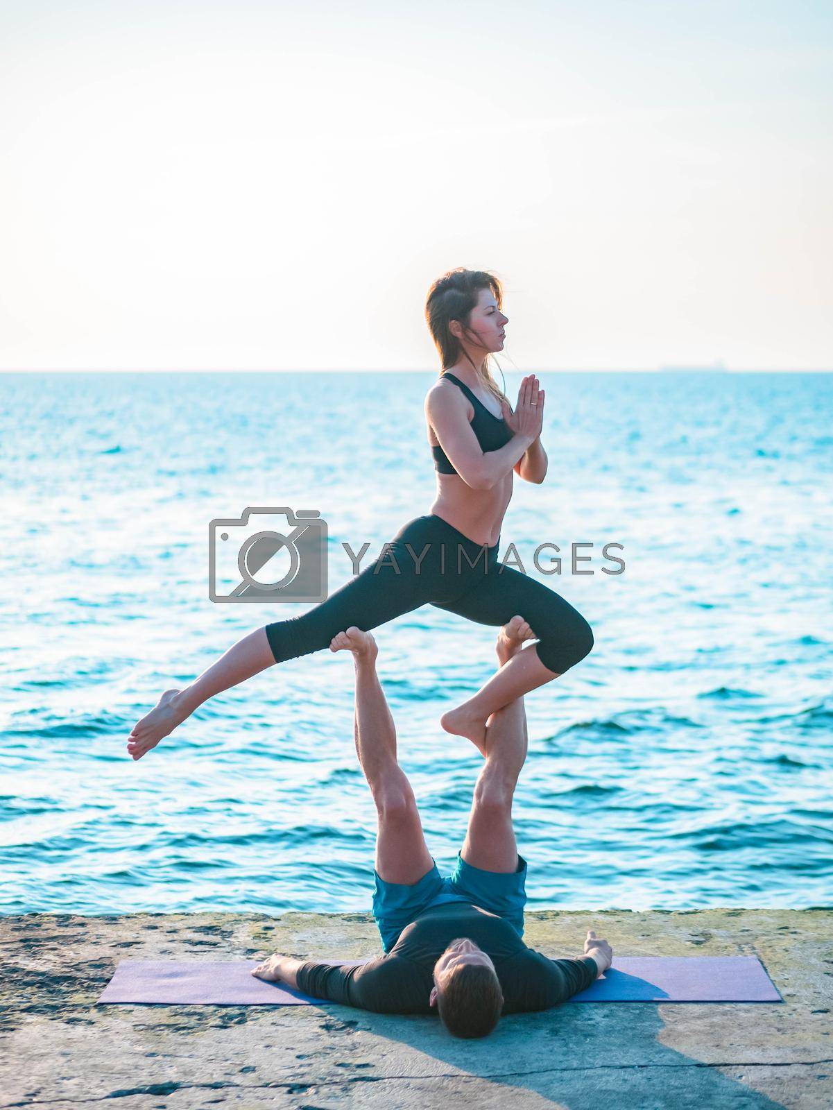 Royalty free image of Young beautiful couple practicing acro yoga on the sea beach near water. Man and woman doing everyday practice outdoor on nature background. Healthy lifestyle concept. by kristina_kokhanova