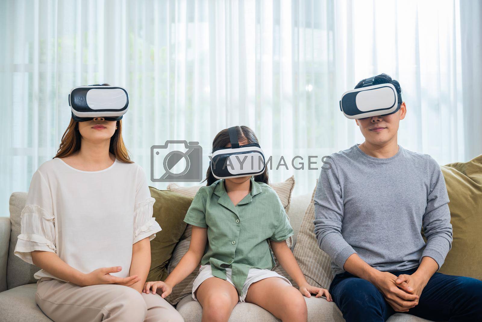 Royalty free image of Asian family wear vr glasses headsets sitting on sofa in living room by Sorapop