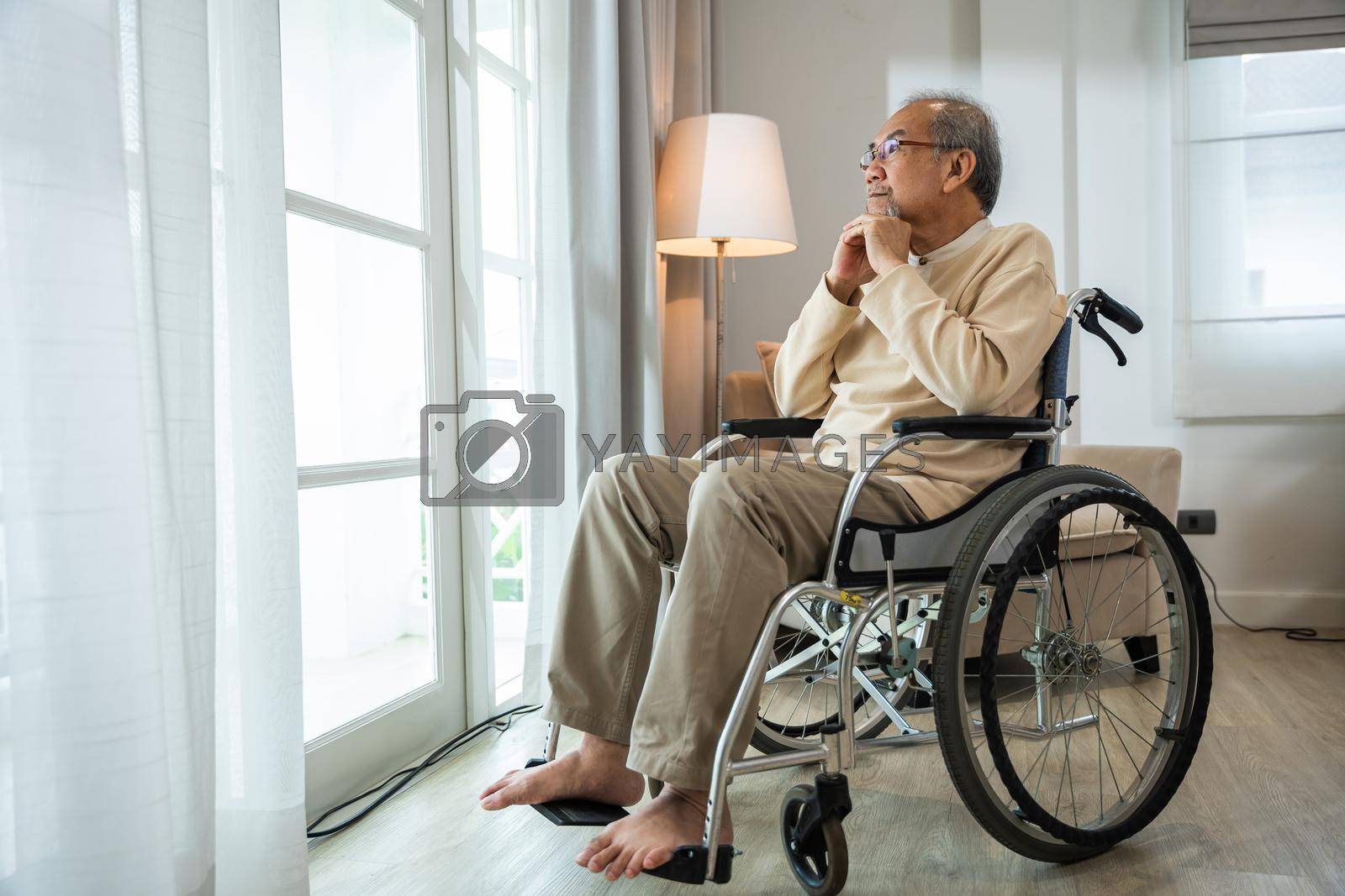 Royalty free image of Asian senior man disabled sitting alone in wheelchair looking through window at hospital by Sorapop