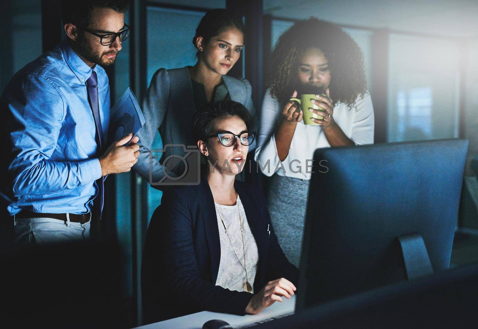 Royalty free image of We think of a deadline as motivation not an obstacle. colleagues standing together as they work on something on a computer at night. by YuriArcurs
