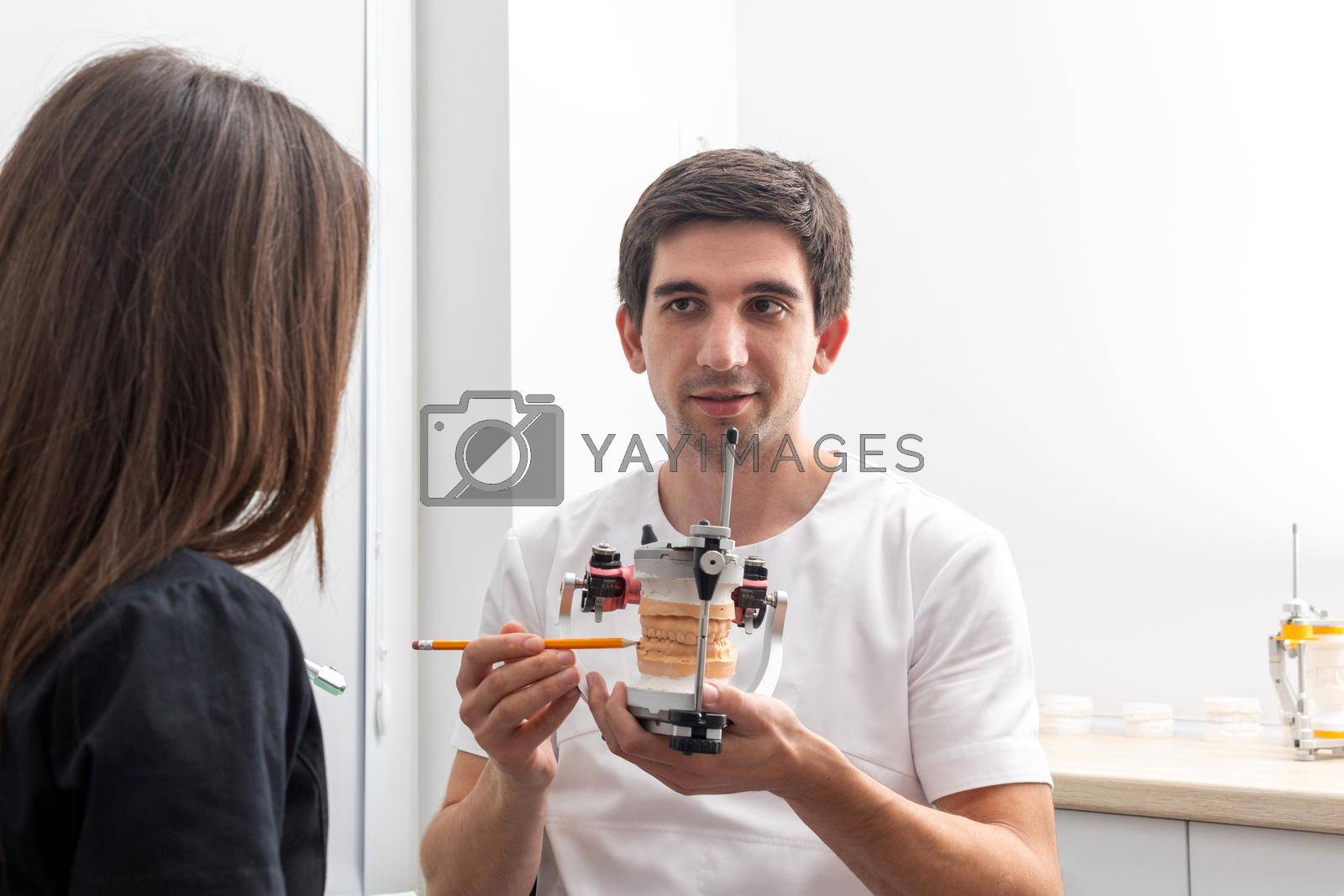 Royalty free image of Dentist holding dental articulator with dental gypsum prosthesis model showing it to a patient by Mariakray