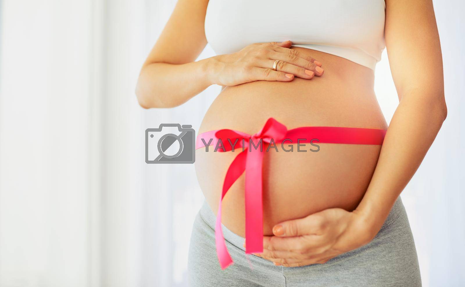 Royalty free image of The most precious gift of all. A little baby girl. a pregnant woman with a pink ribbon tied around her belly. by YuriArcurs