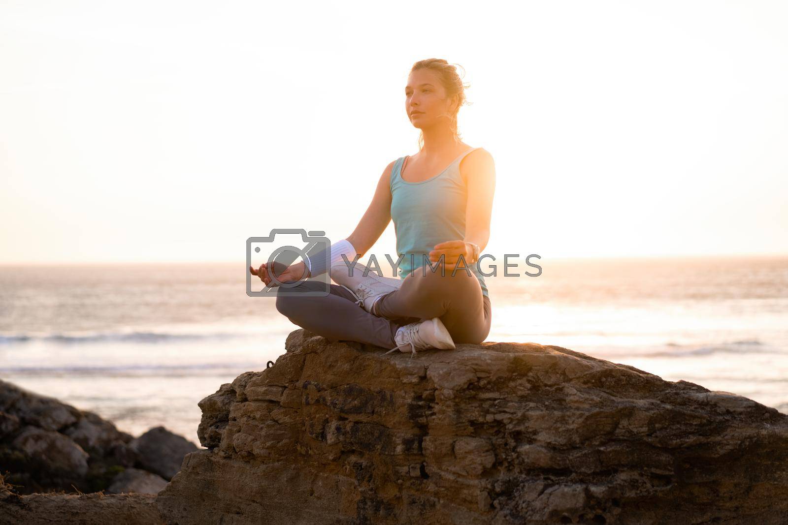 Royalty free image of Woman practice yoga lotus pose to meditation with summer vacation rocky beach happiness and relaxation. Calm female exercise with yoga meditate ocean beach with sunset golden time. by andreonegin