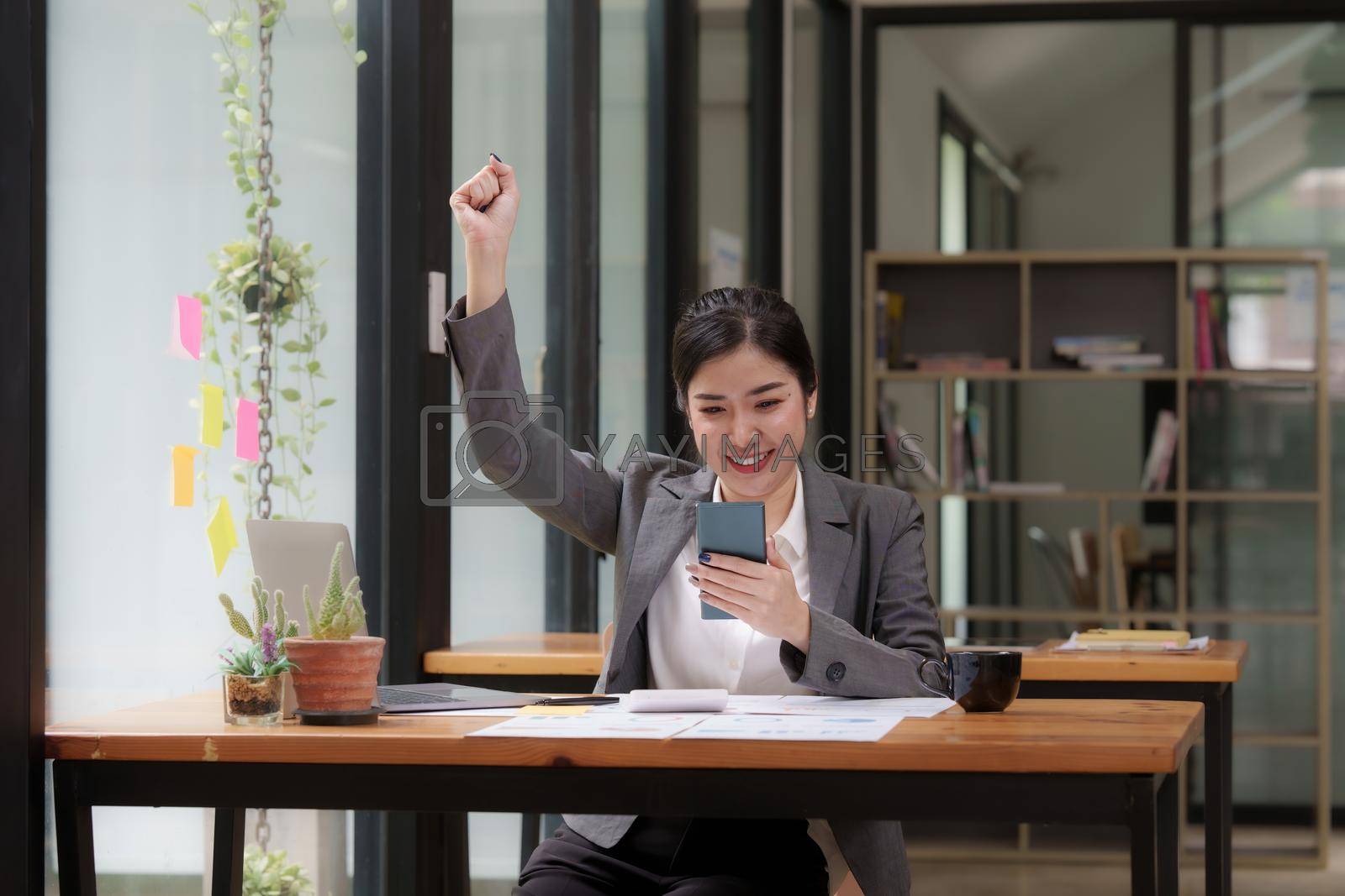 Royalty free image of Happy Asian man using smartphone while have a good news working at office by itchaznong