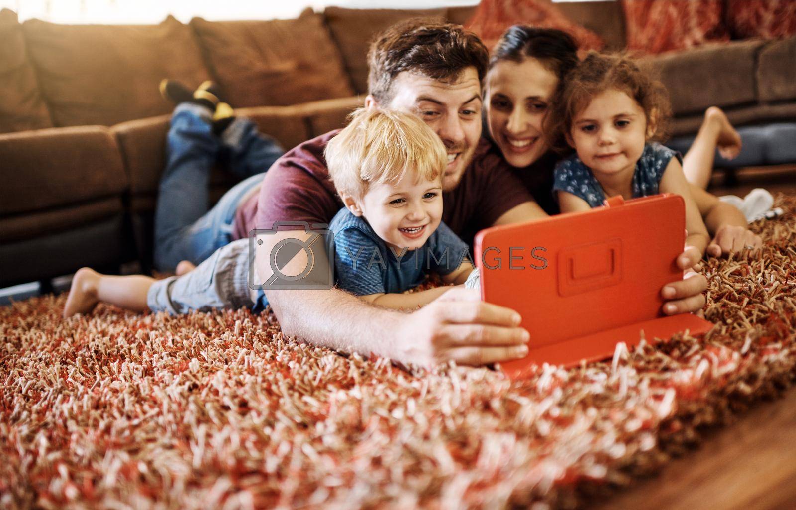 Royalty free image of Theres something online for all ages. a happy young family looking at a tablet together while lying on the carpet in their lounge. by YuriArcurs