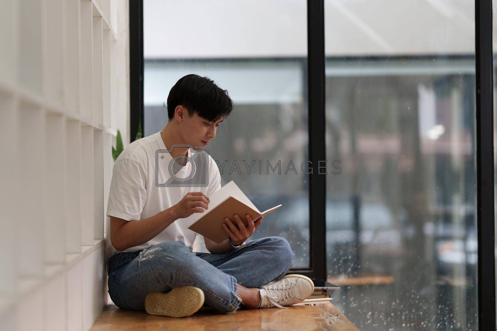 Young Asian man reading a book at cafe. Lifestyle concept.