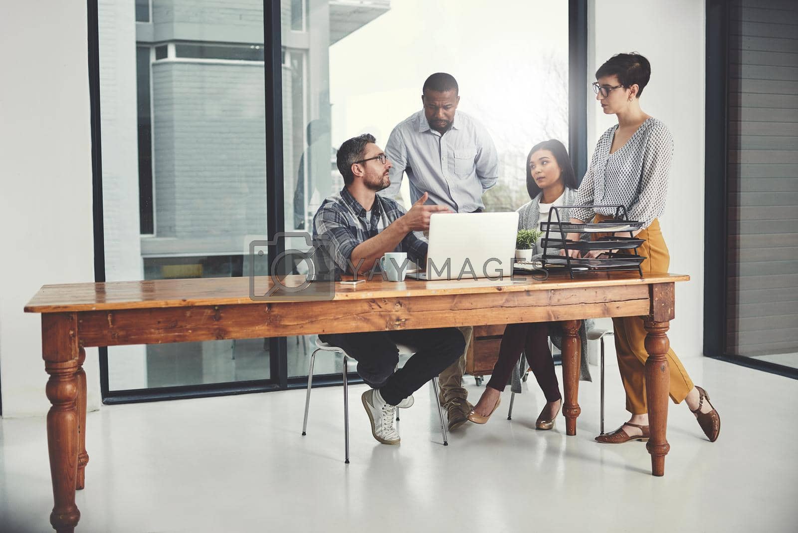 Royalty free image of Working together in the pursuit of success. Full length shot of a group of businesspeople gathered around a laptop in their office. by YuriArcurs