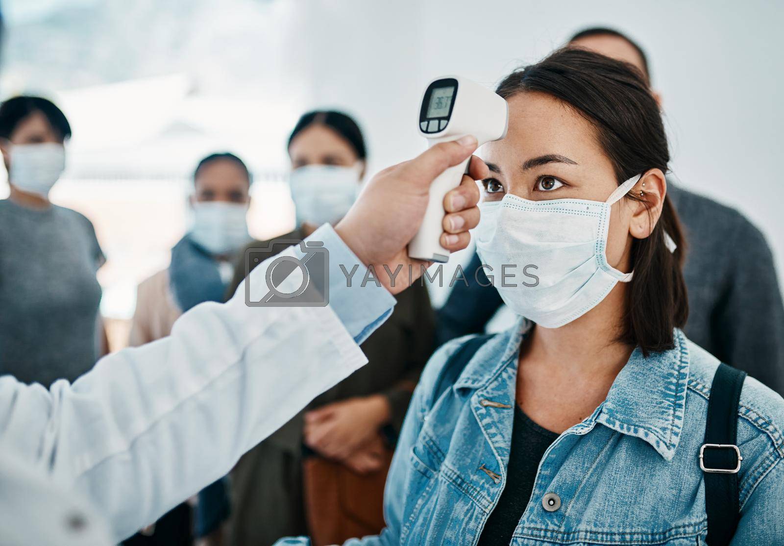 Covid screening with a female tourist in a mask having her temperature taken with an infrared thermometer while waiting to board in an airport. Travel restrictions during the corona virus pandemic.