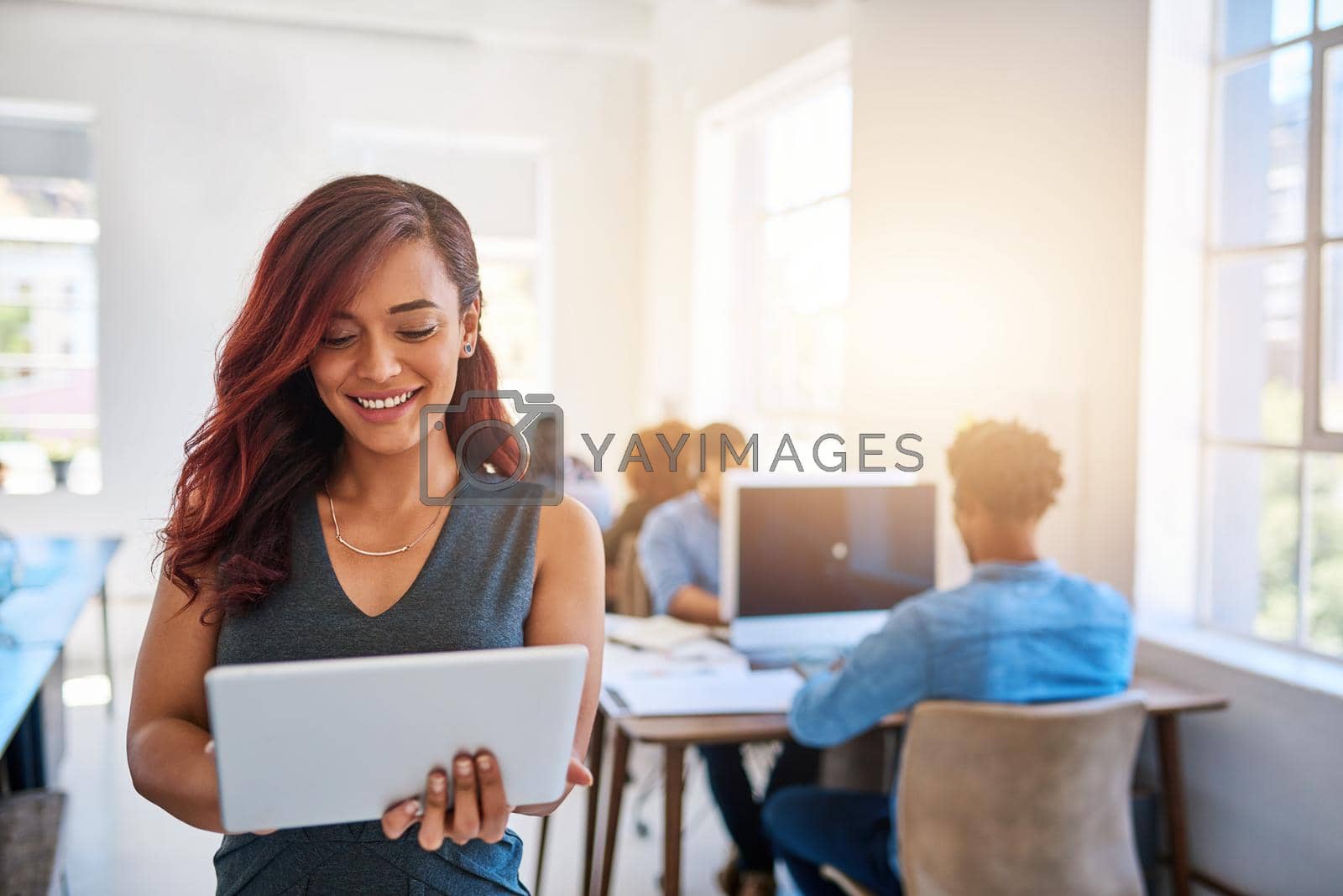 Royalty free image of Smart managers use smart technology. a young entrepreneur using a digital tablet at work with her team in the background. by YuriArcurs