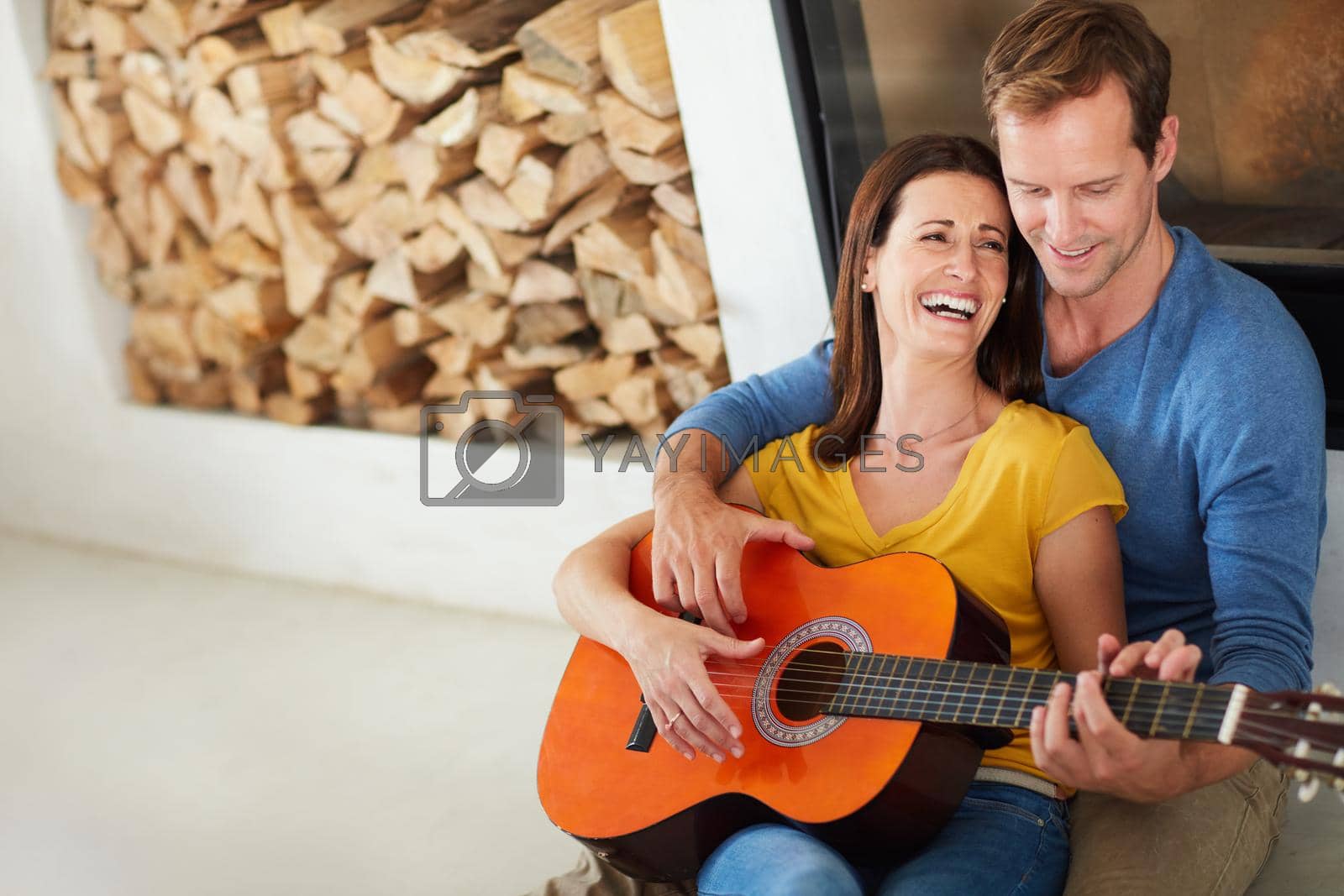 Royalty free image of Nobody else can make her laugh as much as him. a mature couple playing the guitar together at home. by YuriArcurs