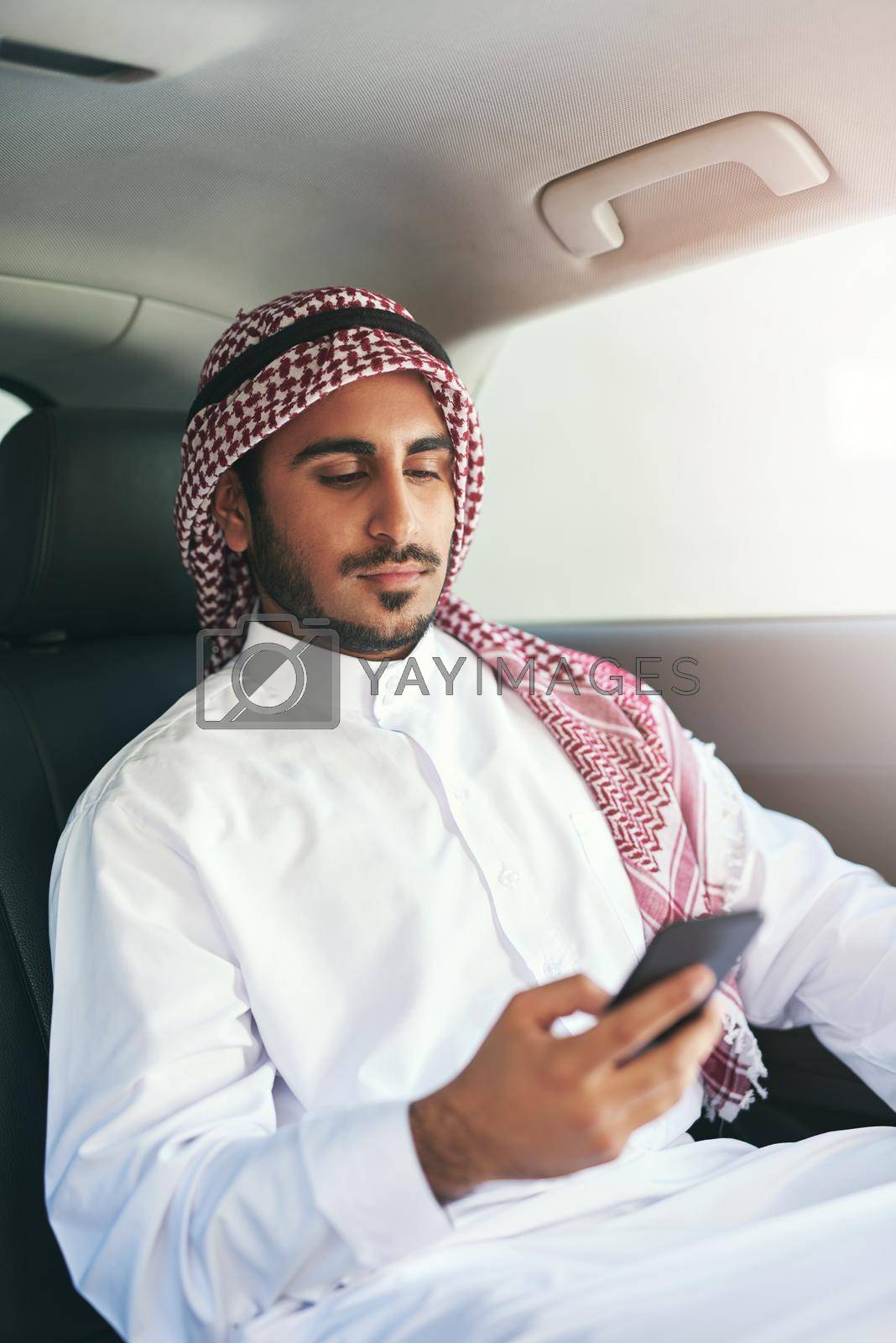 Keeping the lines of communication open. a young muslim businessman using his phone while traveling in a car