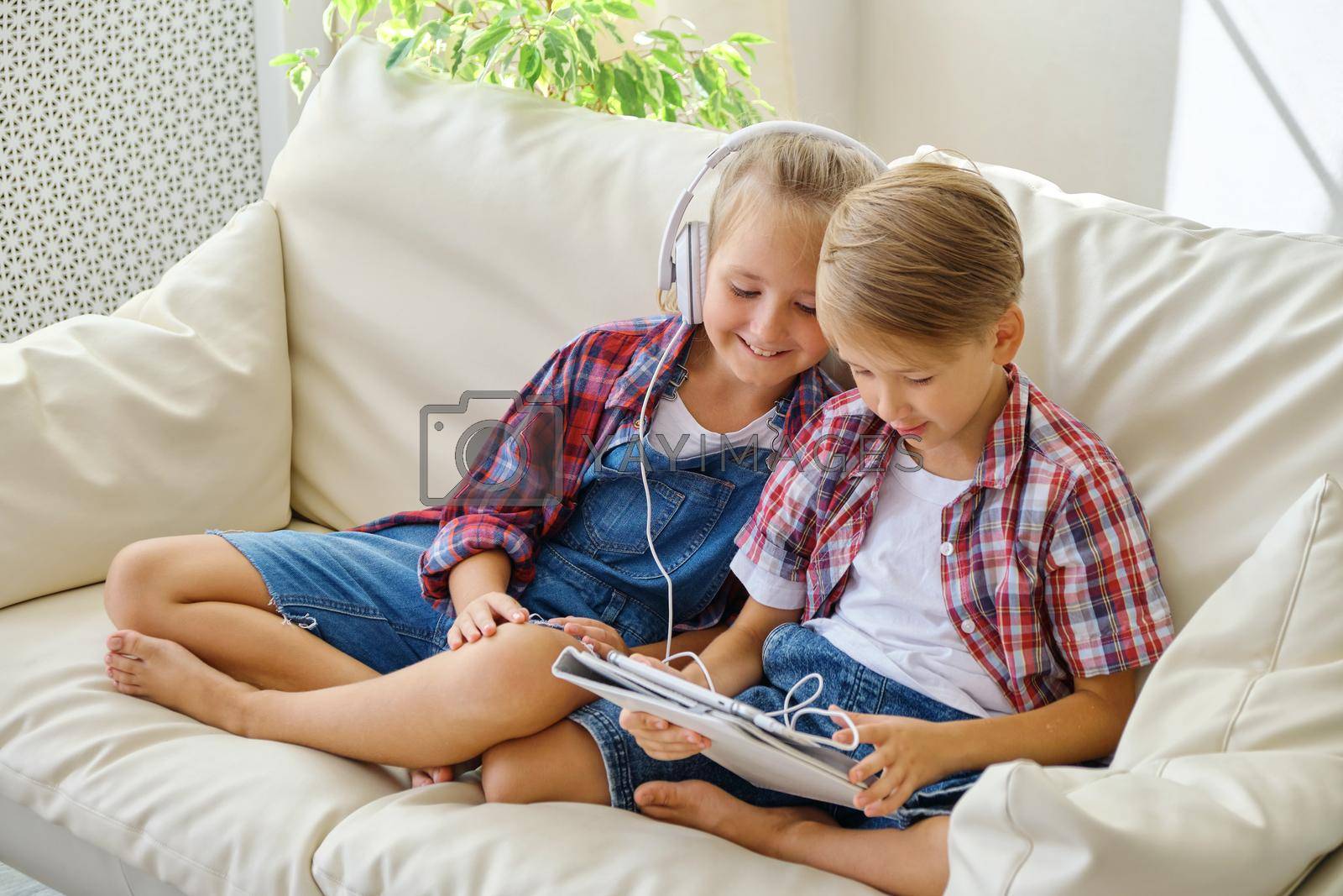 Royalty free image of Cute kids with headphones enjoying tablet at home. by InnaVlasova