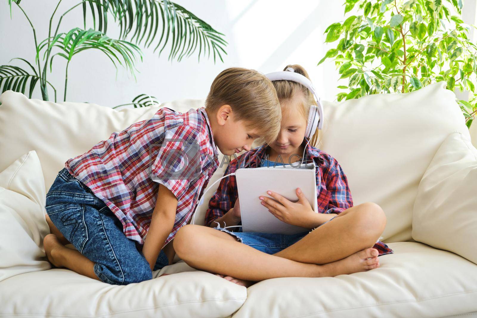 Royalty free image of Cute kids with headphones enjoying tablet at home. by InnaVlasova