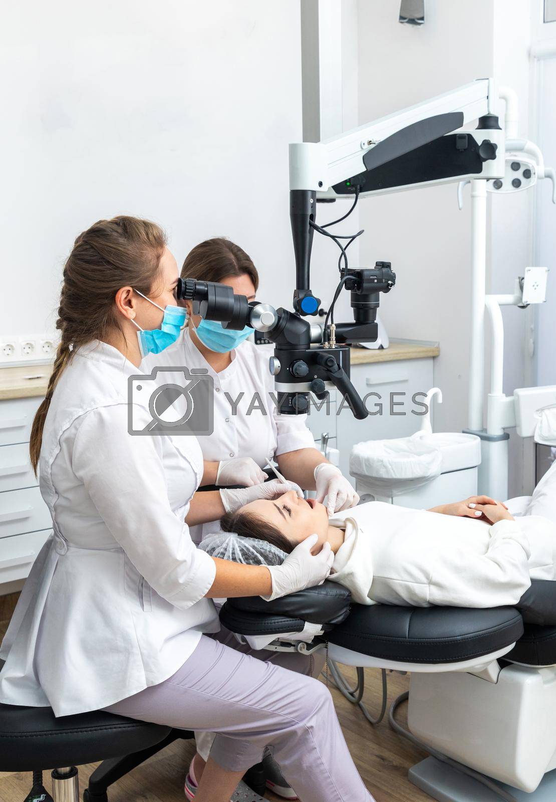 Female dentist using dental microscope treating patient teeth at dental clinic office. Medicine, dentistry and health care concept