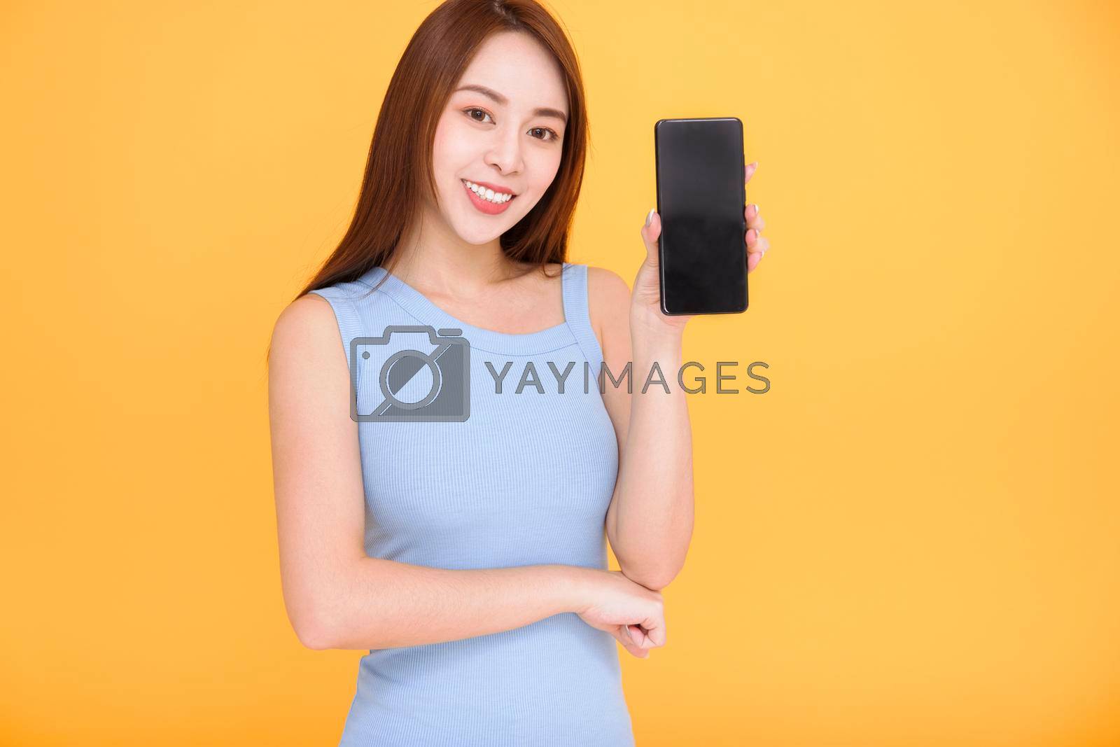 Royalty free image of Smiling asian woman showing mobile phone screen on yellow background by tomwang