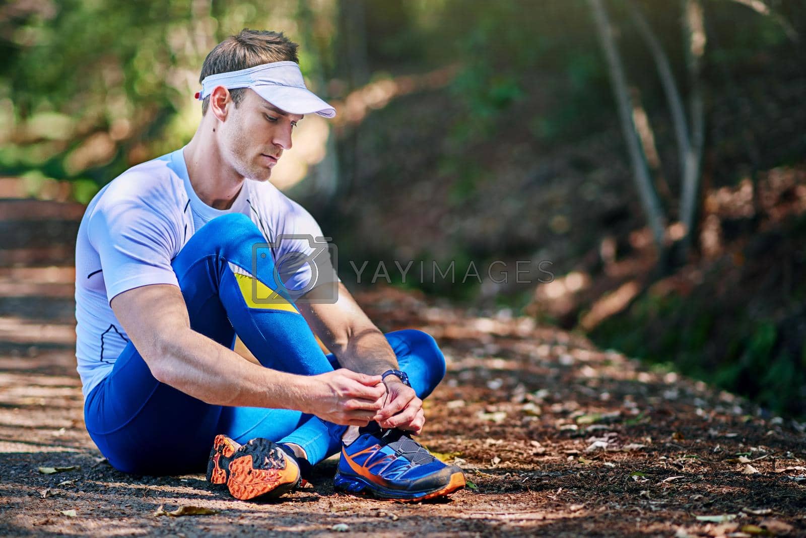Royalty free image of Readying for the run. a young man tying his shoelaces before a trail run. by YuriArcurs