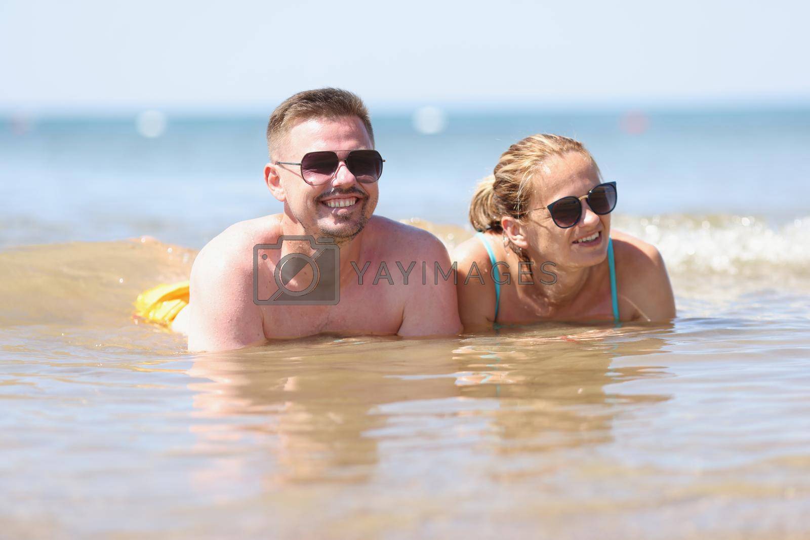 Royalty free image of Happy couple in sunglasses lies on beach in sea by kuprevich