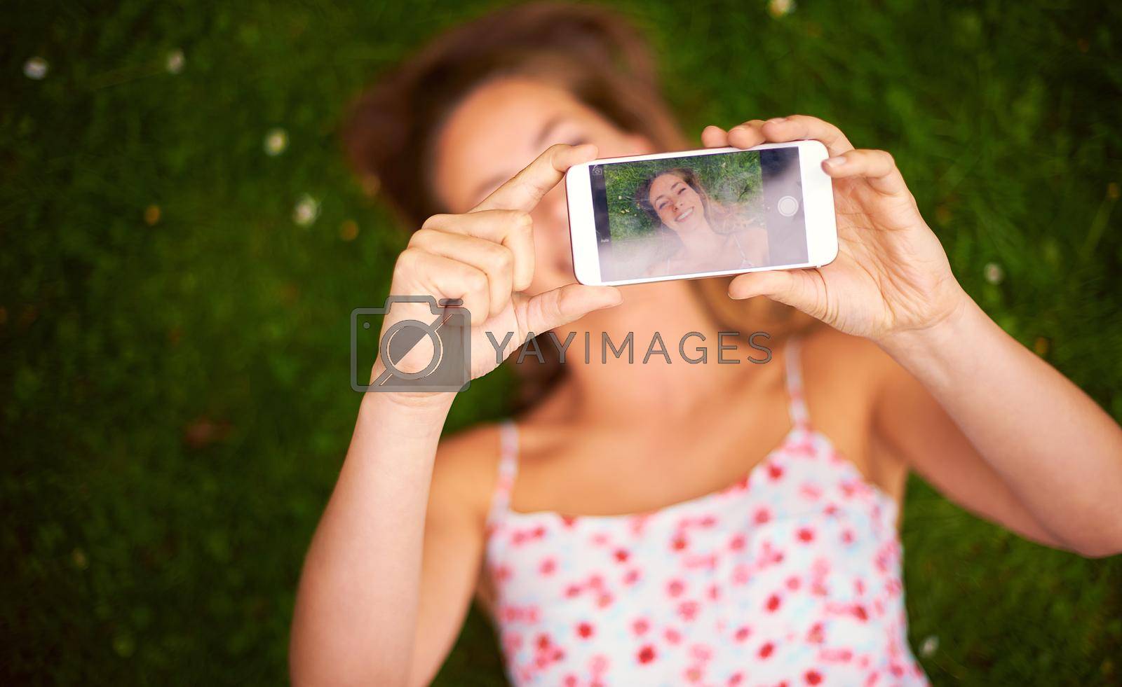 Royalty free image of Taking a summer selfie to share with her friends. a young woman taking a selfie while lying on the grass. by YuriArcurs