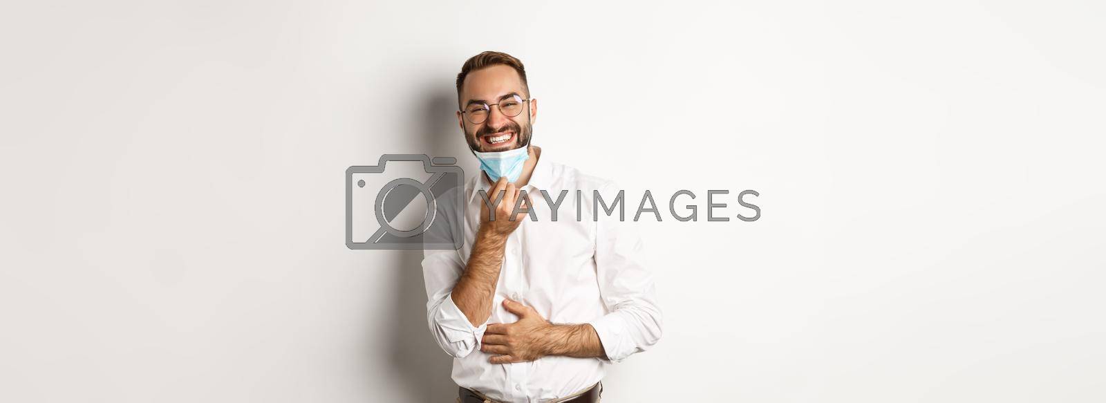 Royalty free image of Covid-19, social distancing and quarantine concept. Happy businessman take off face mask and smiling, standing over white background by Benzoix