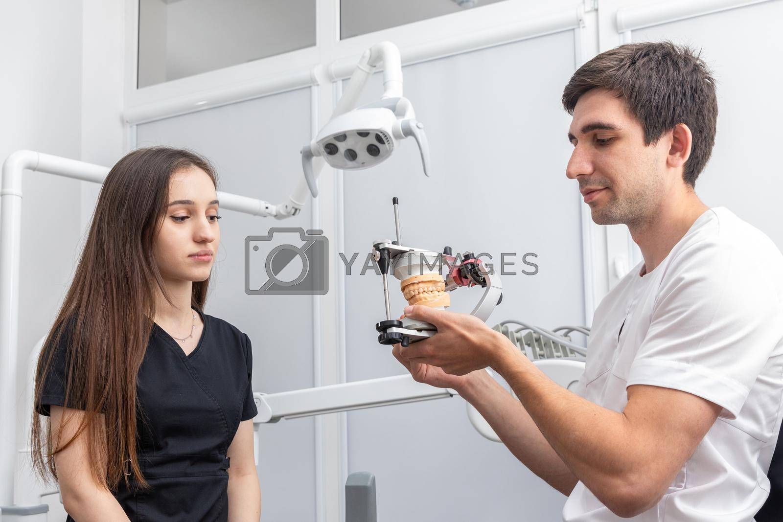 Royalty free image of Dentist holding dental articulator with dental gypsum prosthesis model showing it to a patient by Mariakray
