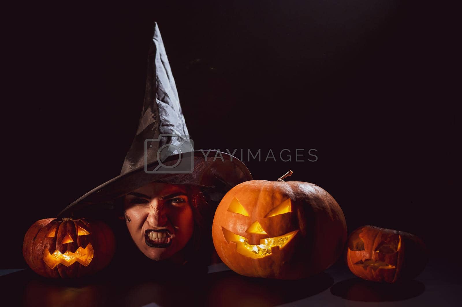 Royalty free image of The head of an evil witch is on the table next to the glowing pumpkin jack-o-lantern by mrwed54