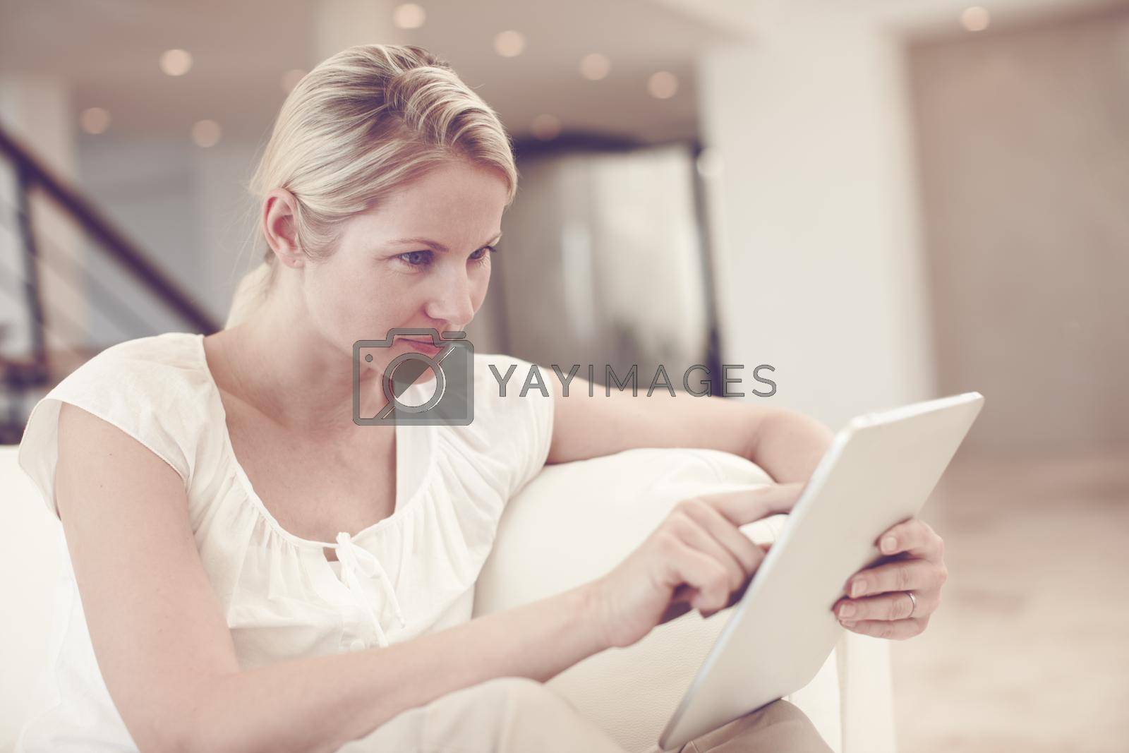 Royalty free image of Reading the news online. An attractive blonde woman using a tablet while sitting at home. by YuriArcurs