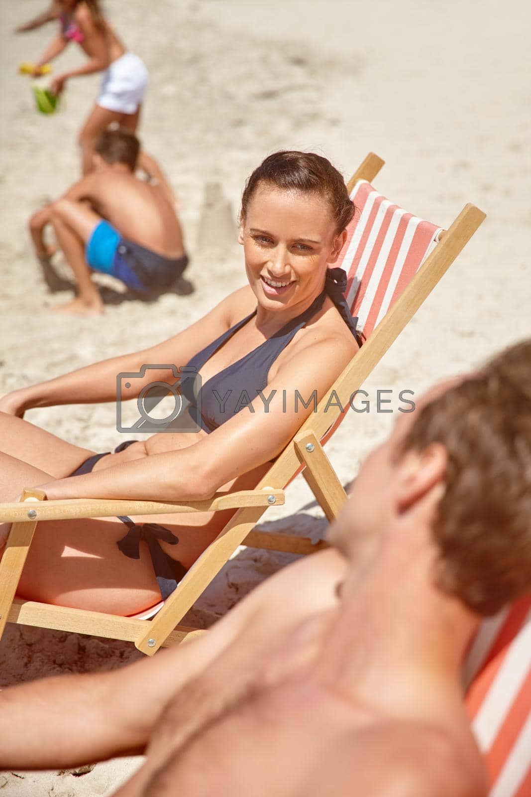 Royalty free image of Sunshine relaxation time at the beach. a couple sitting on beach chairs while their children play in the background. by YuriArcurs