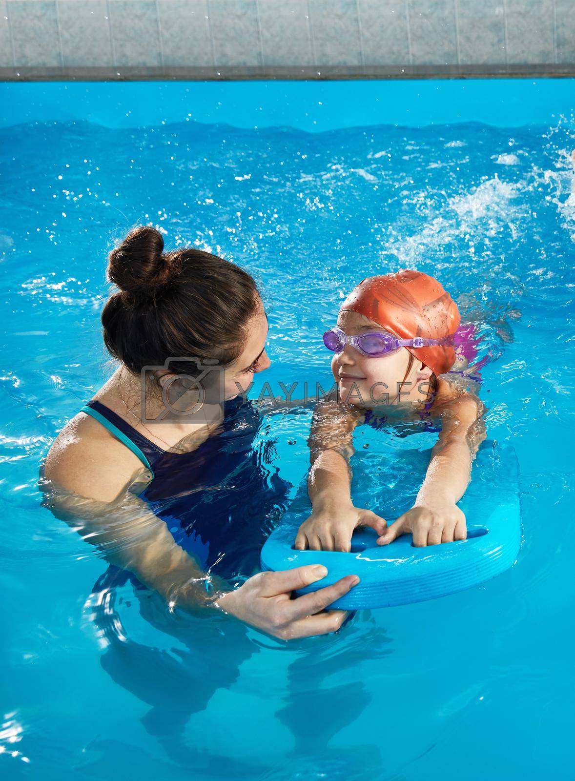 Royalty free image of Little girl learning to swim in indoor pool with pool board and trainer by Mariakray