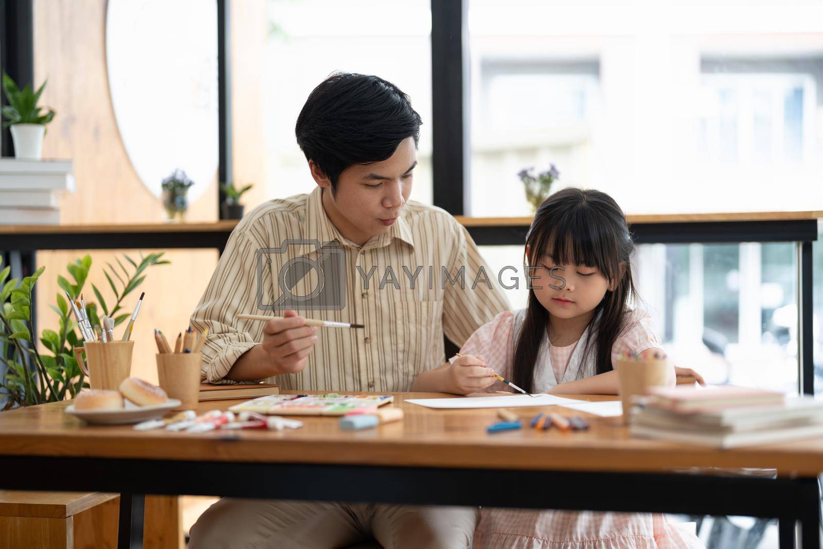 Happy proud asian father and daughter having fun together, drawing and painting watercolor