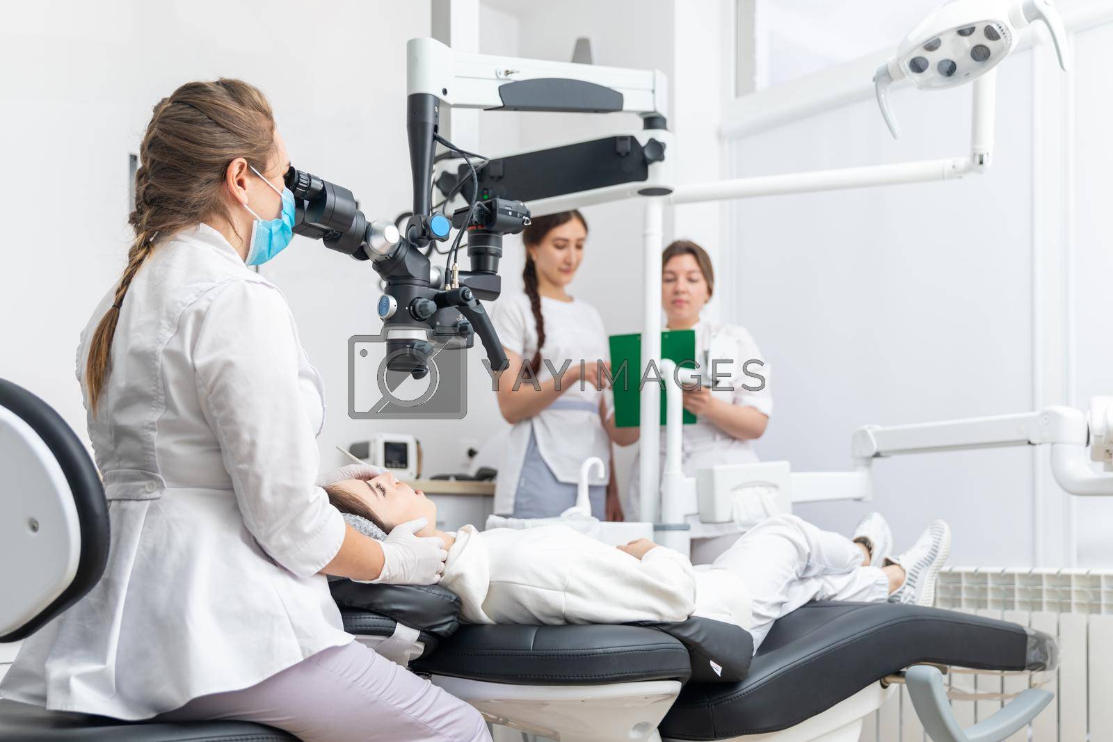 Female dentist using dental microscope treating patient teeth at dental clinic office. Medicine, dentistry and health care concept