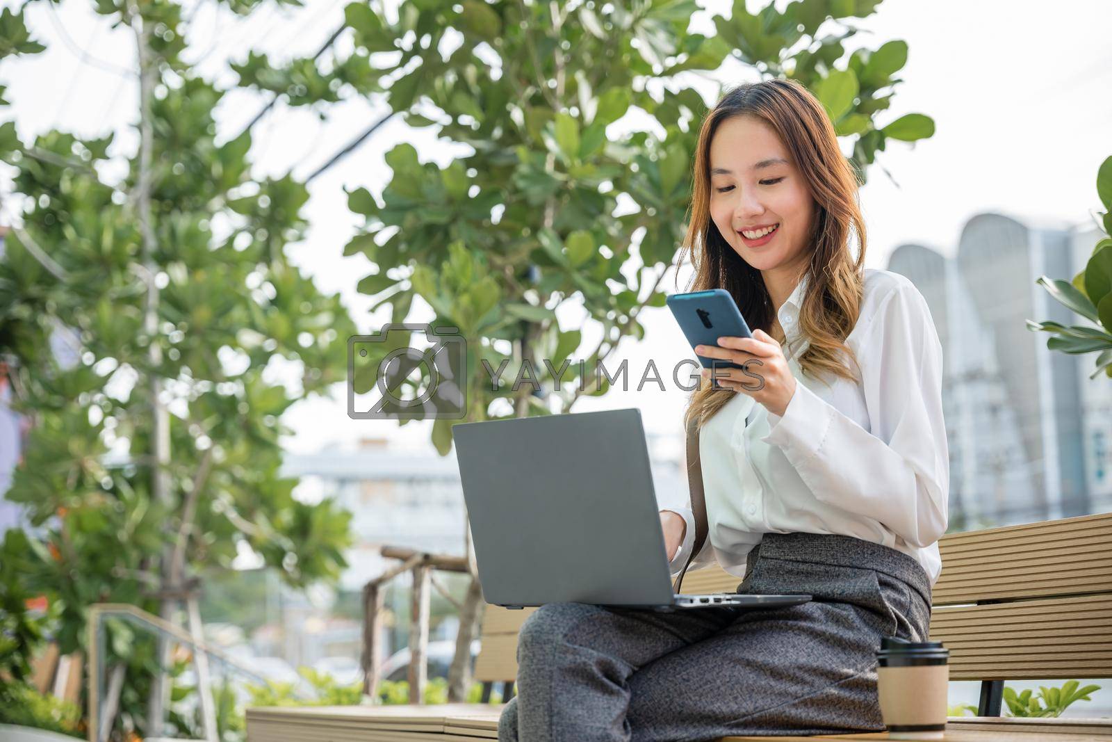 Royalty free image of young woman working laptop and using mobile smartphone outdoor building exterior by Sorapop