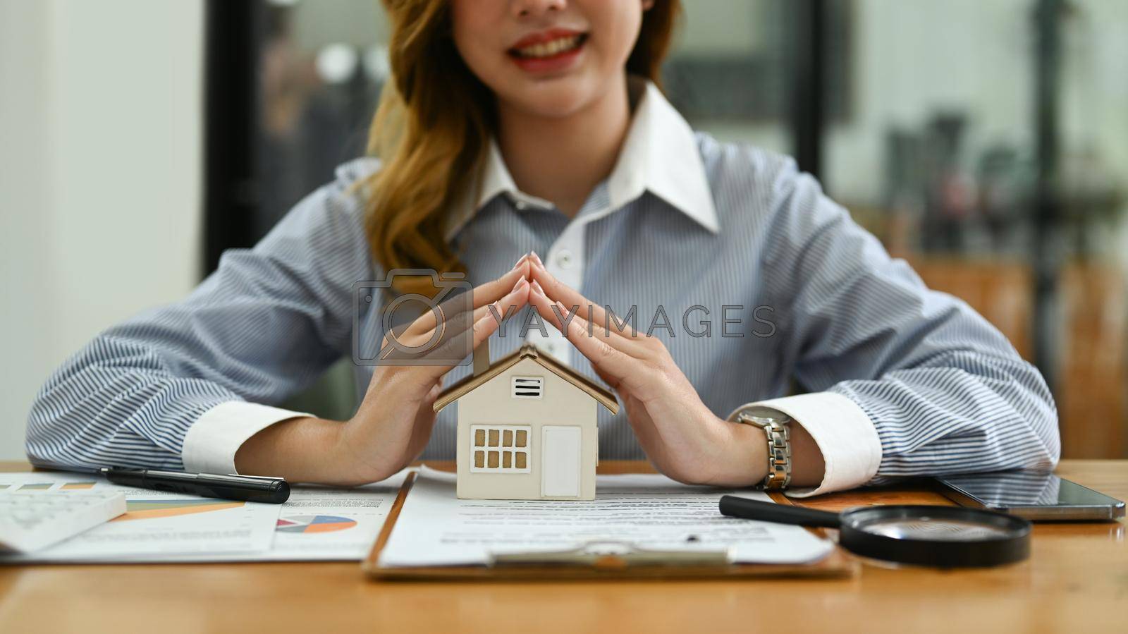 Royalty free image of Smiling woman hands protecting miniature house on wooden desk. Property insurance and reputable financing calm concept by prathanchorruangsak