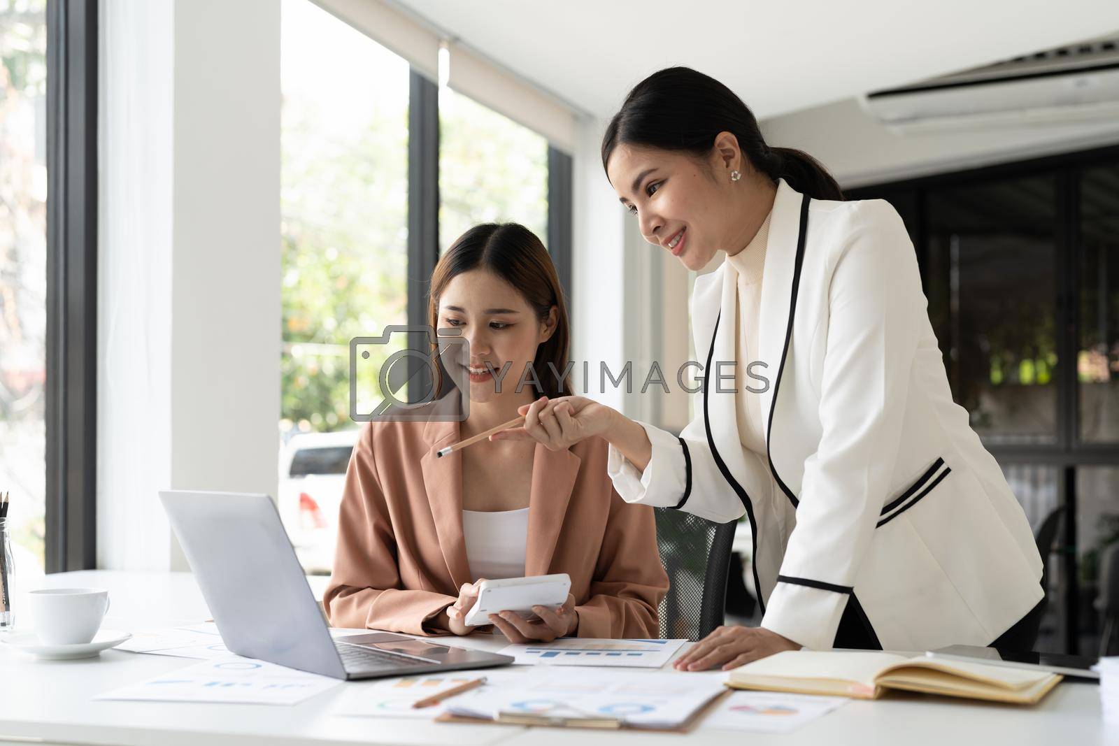 Royalty free image of Young businesswoman adviser standing in front of laptop and giving advise to sales woman. Business people consulting at office. by nateemee