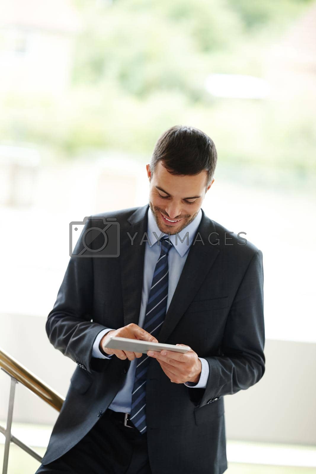 Royalty free image of I cant believe how simple this is. A handsome young businessman using a digital tablet while standing indoors. by YuriArcurs
