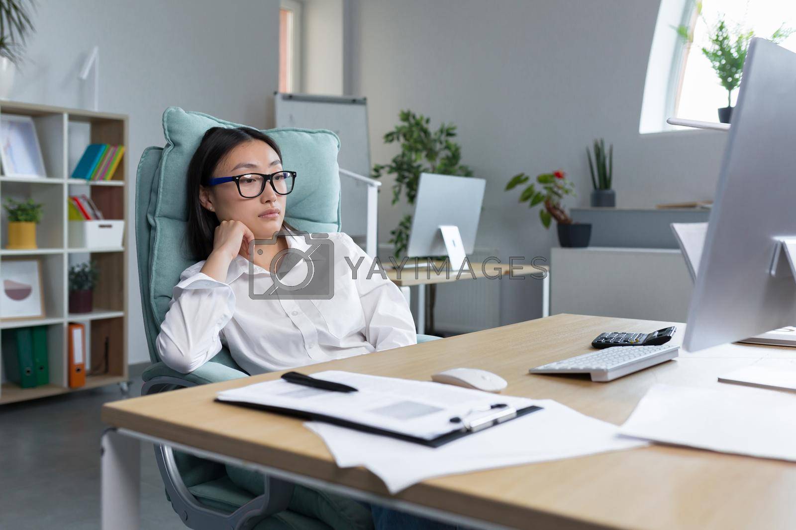 Royalty free image of Pensive and sad young Asian businesswoman sitting in the office at the desk in a big chair by voronaman