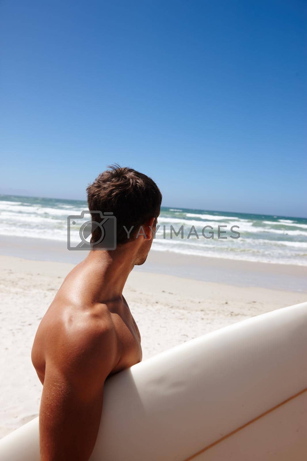 Royalty free image of Perfecting his tan before a surf session. Head and shoulders shot of a young man standing on the beach with his surfboard. by YuriArcurs