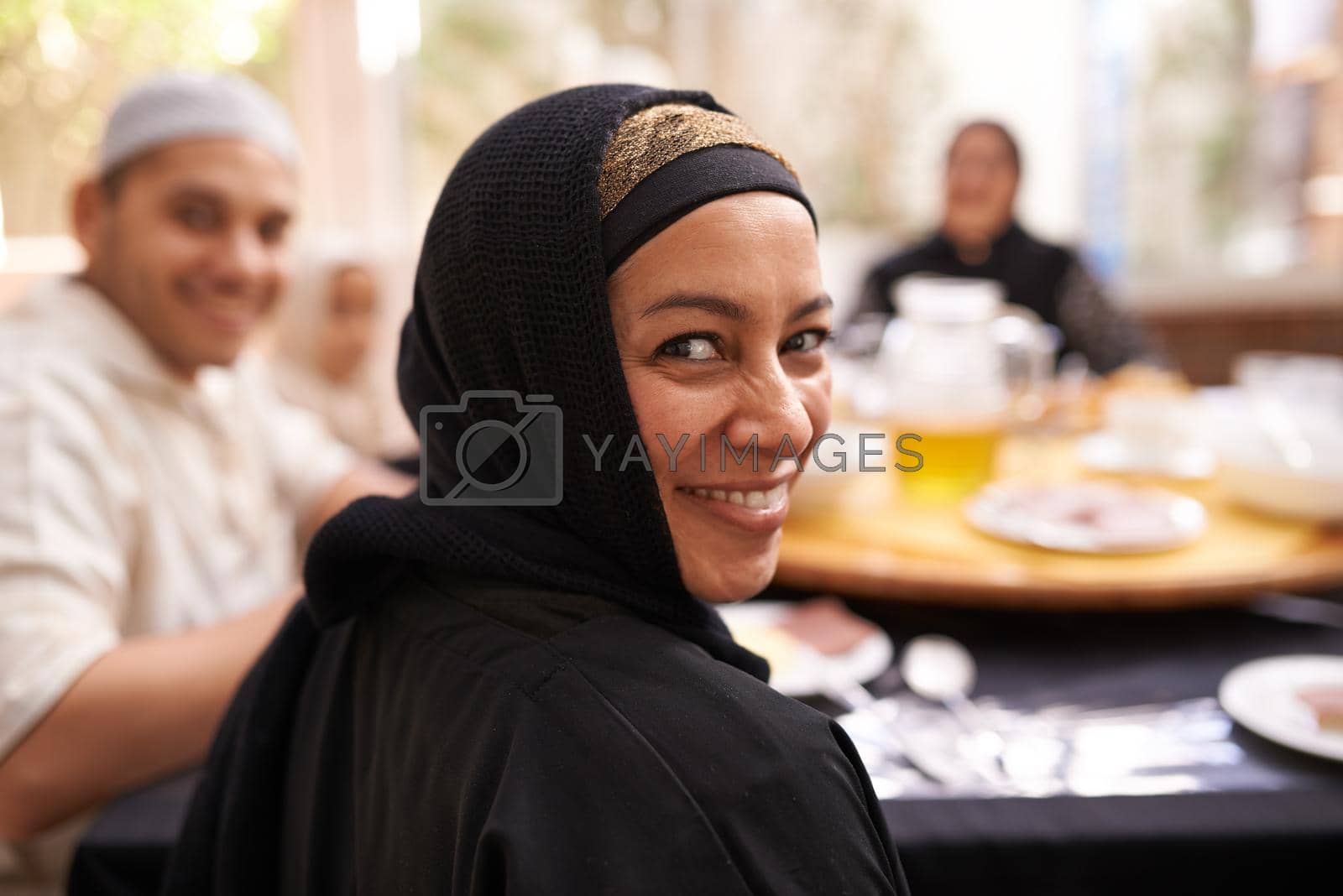 Royalty free image of Hope you brought your appetite. Portrait of a muslim woman looking back while eating with her family. by YuriArcurs