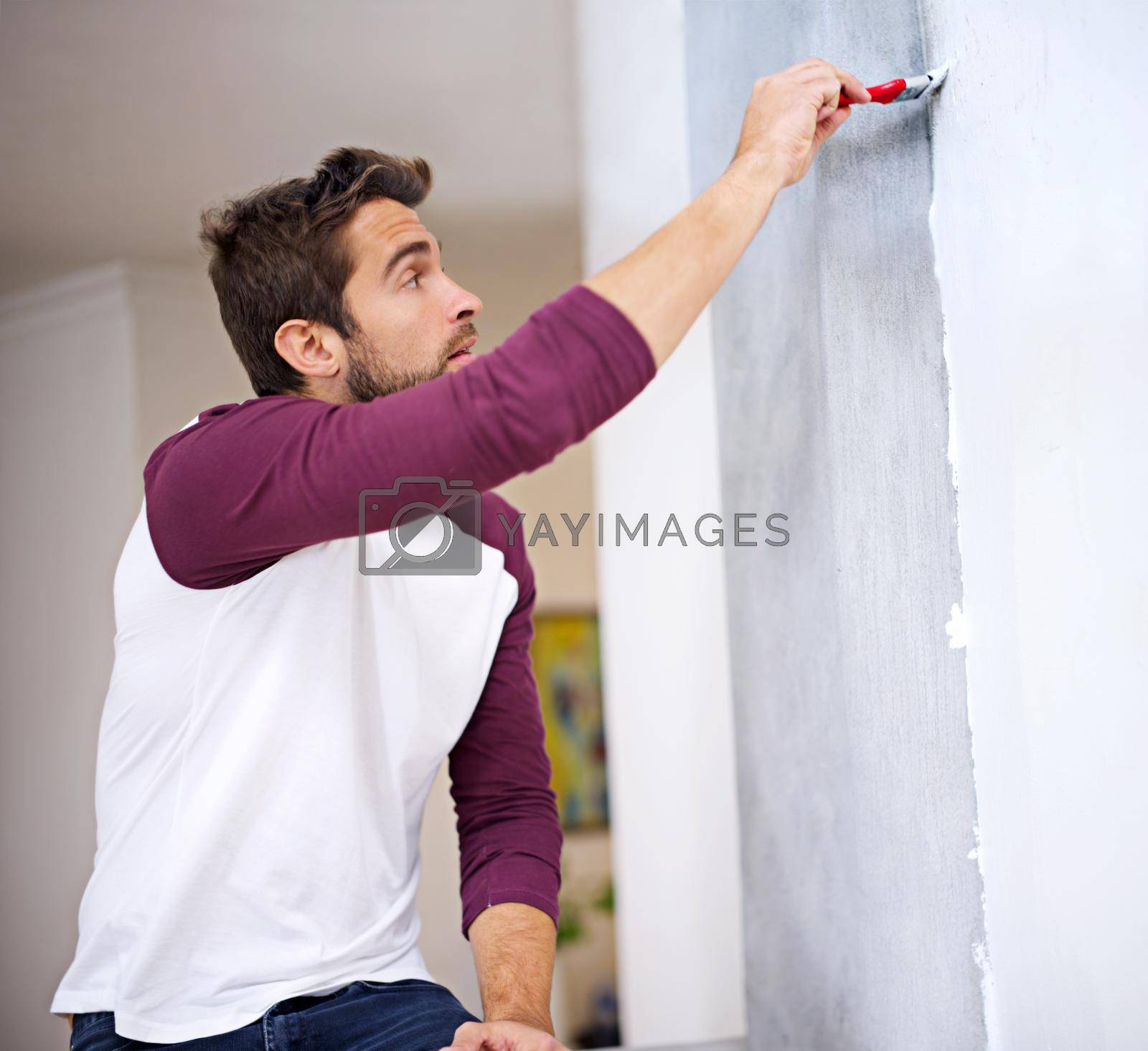 Royalty free image of He wants this to look perfect. Photo of an attractive young man painting a wall indoors. by YuriArcurs