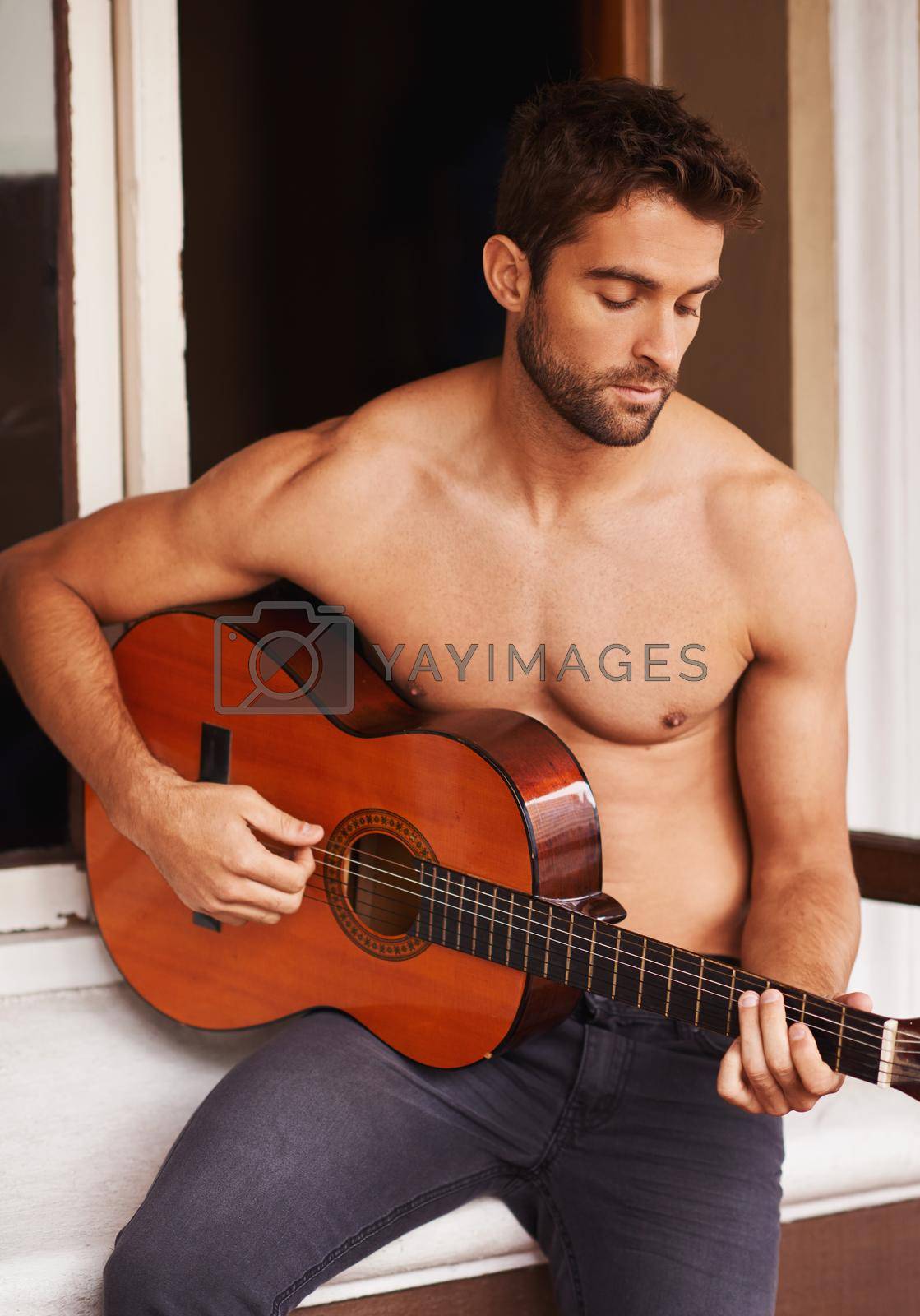 Royalty free image of Playing you a love song. a shirtless young man playing guitar at home. by YuriArcurs