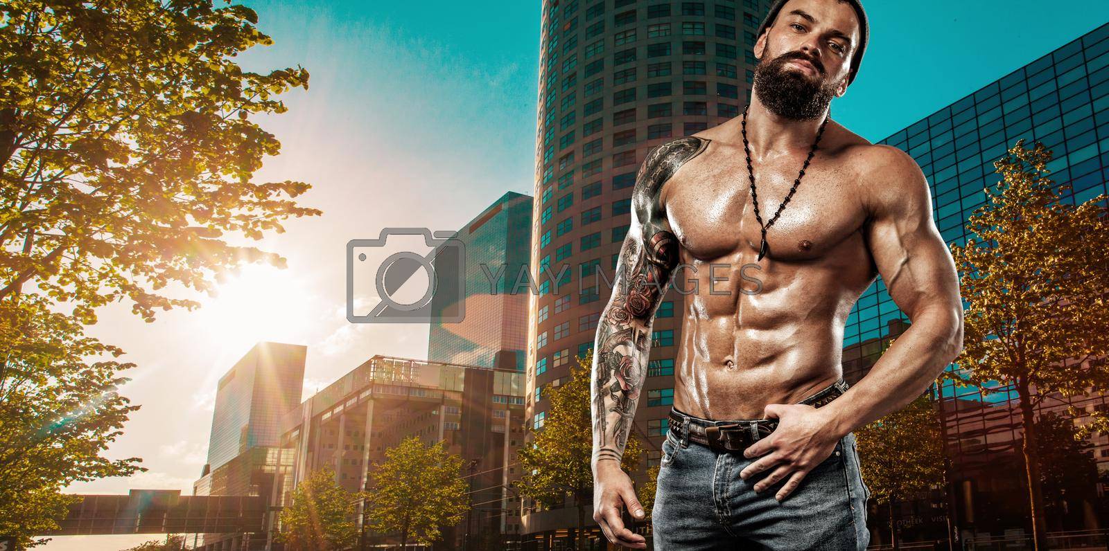 Royalty free image of Handsome fit man posing wearing in jeans with tattoo in the city. Sport and fashion concept. by MikeOrlov