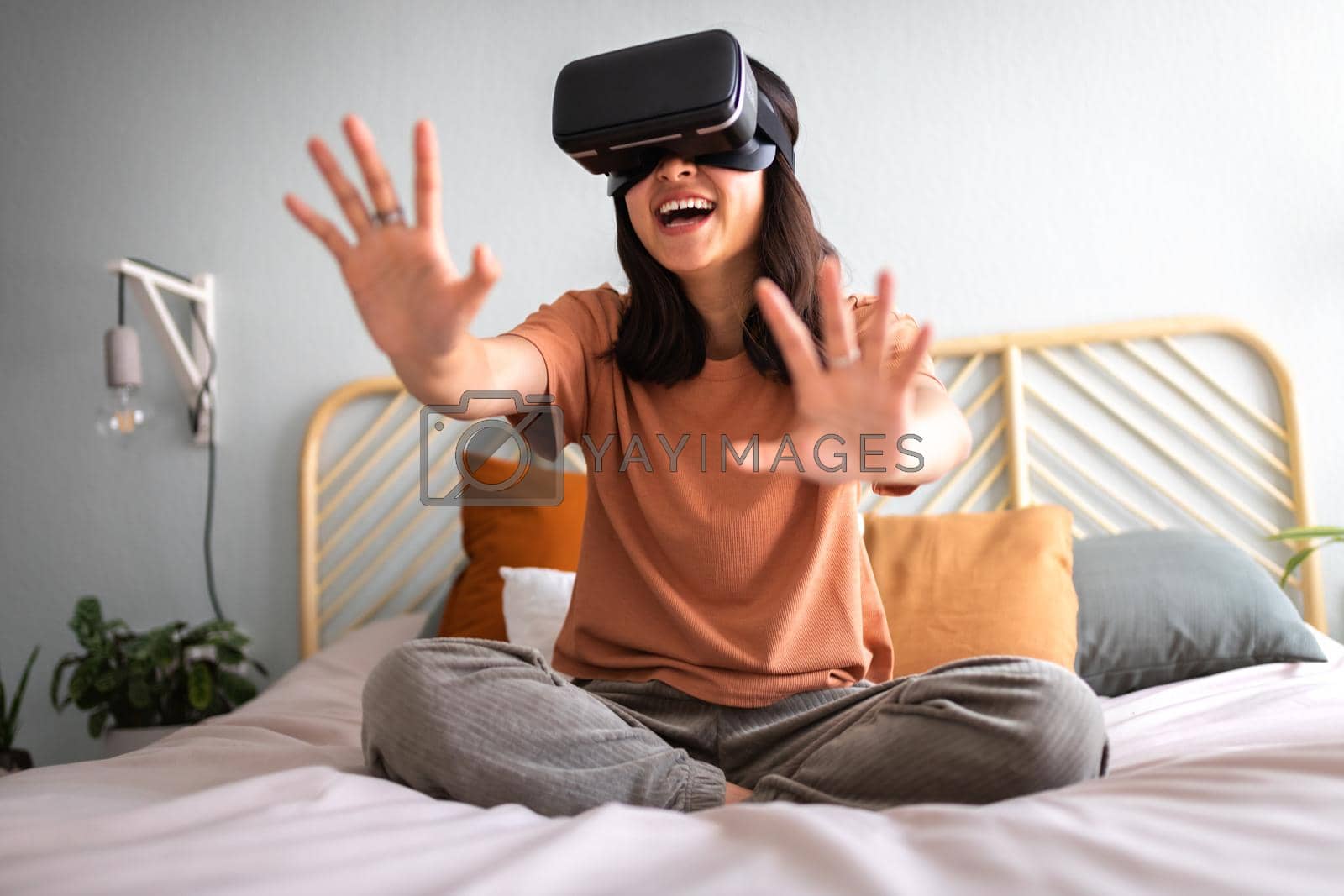 Royalty free image of Happy young asian woman at home moving hands playing simulation video game in virtual reality using VR goggles. by Hoverstock