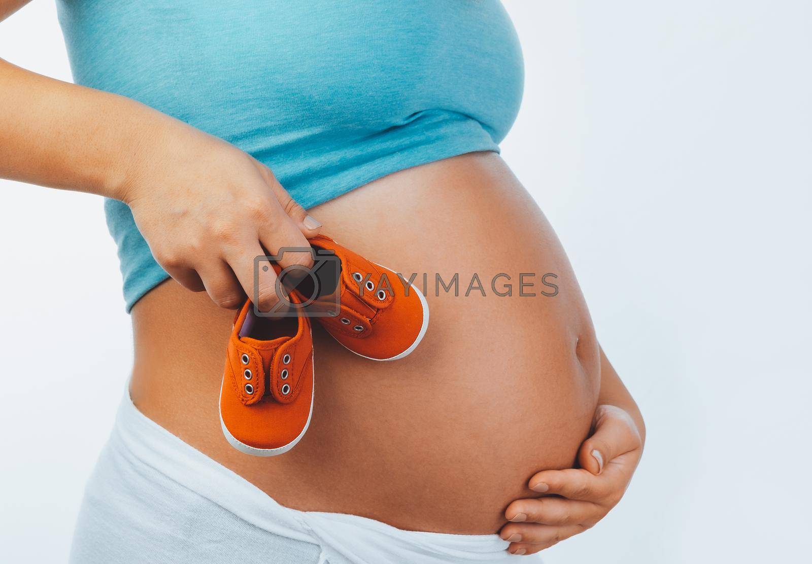 Closeup Photo of a Belly of Expectant Female with Cute Tiny Red Child's Boots isolated on White Background. Family Love Concept.