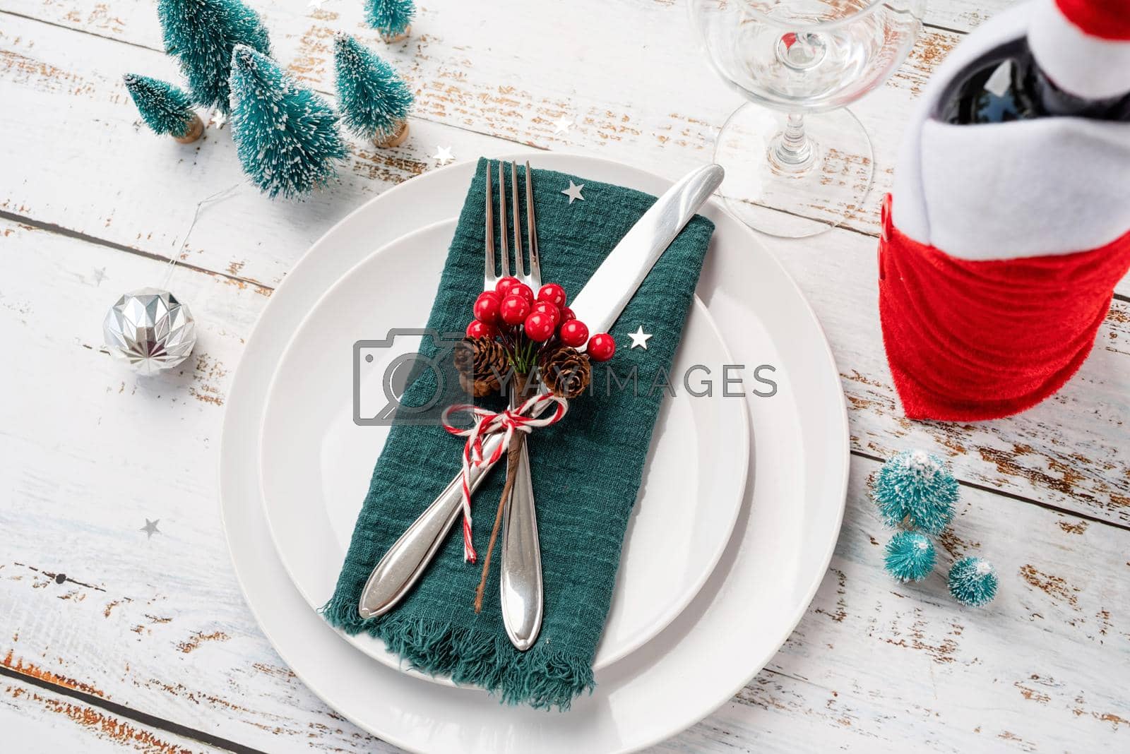 Royalty free image of Christmas table setting with white dishware, silverware and red and green decorations on white wooden background. High angle view. by Desperada